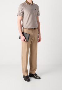 Polo gris avec col marron, pantalon beige et chaussures noires, tenant une tablette noire. Design simple avec des accents minimaux.