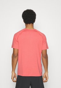 Camiseta atlética de manga corta en color coral, con una textura suave, escote redondo y mangas raglán en contraste. Vista trasera, sin gráficos.