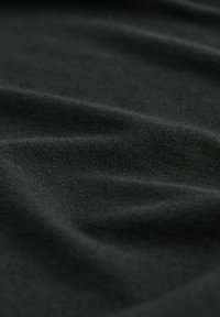 Primo piano di un tessuto nero e liscio con una sottile texture, che mostra morbide pieghe e drappeggi, trasmettendo un senso di eleganza e semplicità.