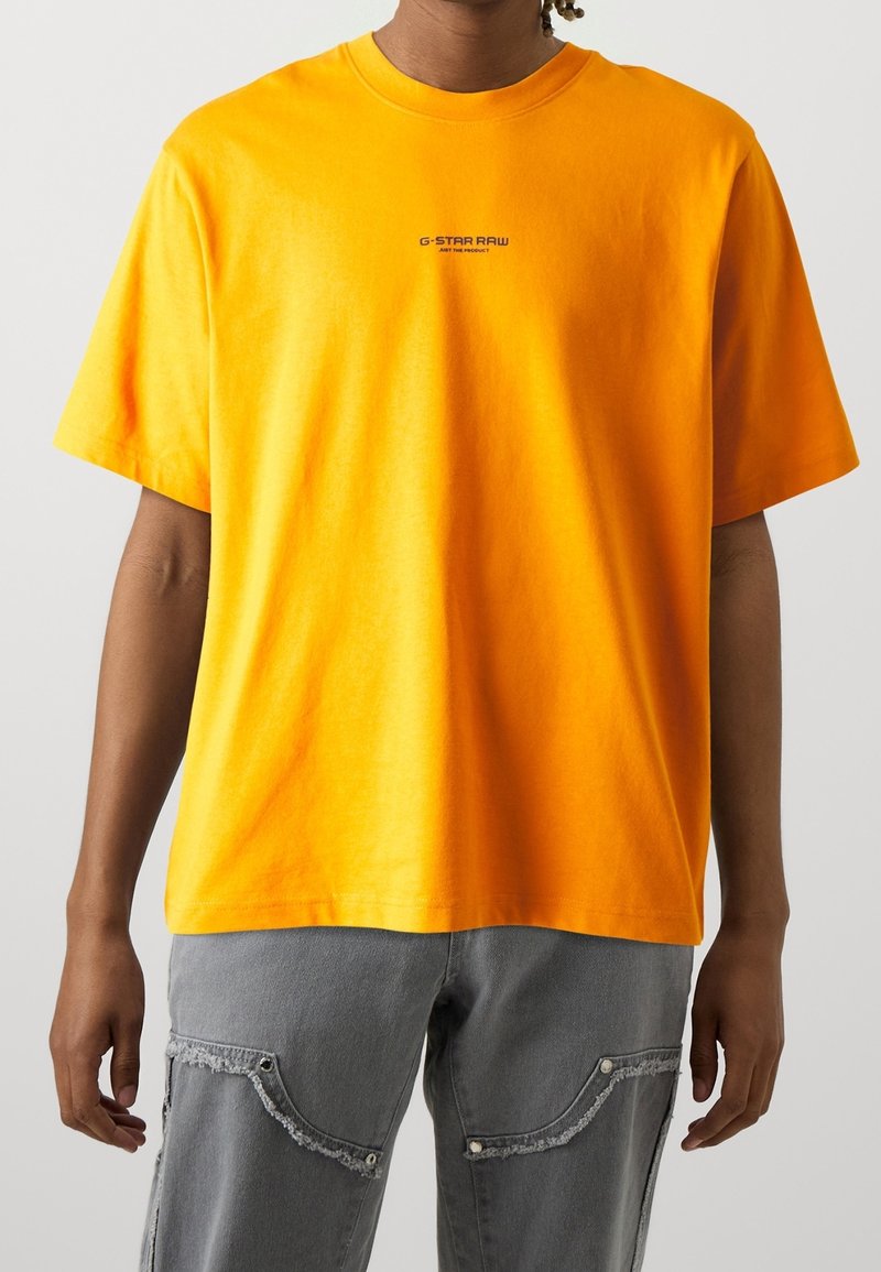 Světlý oranžový bavlněný tričko s kulatým výstřihem a krátkými rukávy. Na hrudi se nachází malé černé logo "G-STAR RAW".