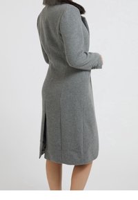 Abrigo gris entallado con cuello de piel, mangas largas y una abertura lateral. Tejido texturizado con un silueta ajustada y puños abotonados.