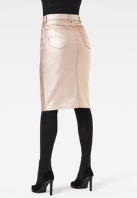 Rosa Satin-Bleistiftrock mit Gesäßtaschen und Nähdetails, kombiniert mit schwarzen Strumpfhosen und schwarzen Stiefeletten mit Absatz.