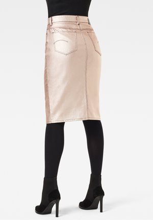 Jupe crayon en satin rose clair avec poches arrière et détails de couture, accompagnée de collants noirs et de bottines à talons noirs.