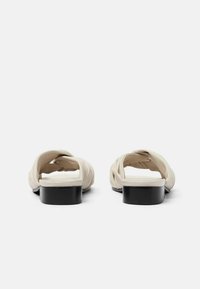 Sandali open-toe beige con design superiore attorcigliato, dotati di un basso tacco a blocco nero e una superficie liscia.