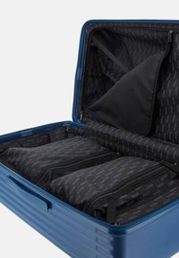 Valigia rigida blu con un esterno resistente. L'interno presenta scomparti con cerniera nera e tasche organizzative con motivo del logo.