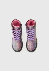 Bottines à paillettes violettes avec des motifs de cœurs multicolores, lacées de violet et doublées de fourrure rose. Semelle en caoutchouc noir épais.