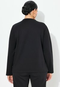Maglietta nera a maniche lunghe con scollatura arrotondata, texture liscia, vestibilità rilassata e sottili spacchi laterali all'orlo.