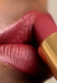 Matte lippenstift aangebracht op volle lippen met een warme roze tint. De textuur lijkt glad met fijne lijntjes zichtbaar op de lippen. Gouden buisdetaillering zichtbaar.