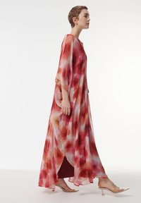 Lang, vloeiende jurk van lichtgewicht stof met een aquarelpatroon in rood, roze en oranje tinten. Losse mouwen en een zijsplit.
