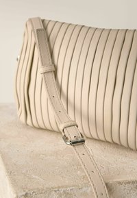 Borsa a mano in pelle beige con texture plissettata verticale, tracolla regolabile e dettagli in metallo. Finitura liscia con cuciture discrete.