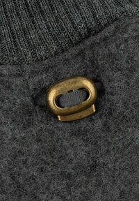 Dunkelgrauer Stoff mit einer weichen Textur, der ein bronzenes ovales Hardwareelement und eine Kordelschlaufe in einem kontrastierenden Farbton aufweist.