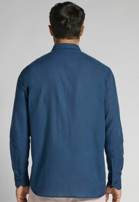 Mörkblå skjorta med långa ärmar, med klassisk krage och knäppning i ärmsluten. Slät yta med ett subtilt, enhetligt mönster.