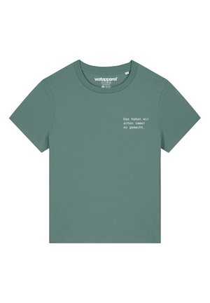 Groene katoenen t-shirt met korte mouwen. Het ontwerp aan de voorkant heeft witte tekst: "Das haben wir schon immer so gemacht." Ronde hals.