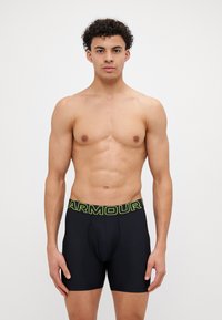 Čierne boxerky z pružného materiálu, s hrubým neónovo zeleným pásom so slovom 'ARMOUR' vytlačeným na ňom. Hladký povrch a priliehavý strih.