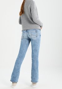 Jasnoniebieskie dżinsy w fasonie dzwonów z wyblakłym wykończeniem, pięcioma kieszeniami i haftowanymi tylnymi kieszeniami; zestawione z szarym swetrem i białymi butami.