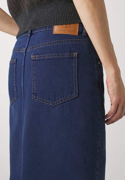 Mørkeblå denimskjørt med to baklommer og oransje sømmer. Har en tan-lær etikett med merkevarenavnet i midjen.
