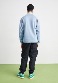 Vaaleansininen collegepaita raglanhihoilla, yhdistetty mustiin cargo-housuihin taskuilla. Jalkineina vihreät ja valkoiset tennarit.