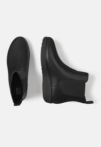 Schwarze Stiefeletten aus glattem Synthetikmaterial mit elastischen Seitenpanelen und einer strukturierten Gummisohle für besseren Halt. Minimalistisches Design mit Ziehhilfe.