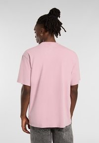 Rosa T-shirt med kort ärm och rund hals, gjord av mjuk bomull. Har en avslappnad passform och rak fåll, bärs med grå jeans.