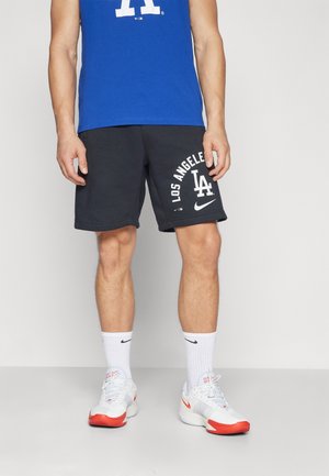 Camiseta sin mangas azul con logotipo de "LA", pantalones cortos negros con la impresión "LOS ÁNGELES", calcetines blancos y zapatos blancos con detalles en rojo.