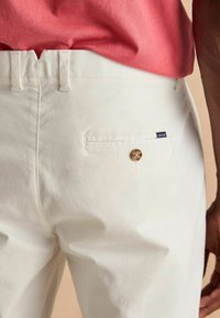 Valged puuvillased püksid sisaldavad tagakotti, millel on nupuga lukustus ja väike sinine silt, millel on kirjutatud "JOULES". Kanga pind näeb välja sile ja mati viimistlusega.