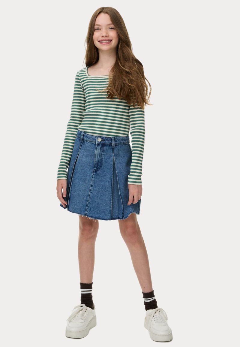 Maglietta a maniche lunghe a strisce verde e bianco abbinata a una gonna di jeans blu con orlo sfrangiato e pieghe frontali. Indossata con sneaker bianche.