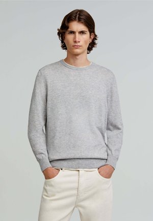 Light gray knitted sweater with a round neckline, long sleeves, and ribbed cuffs, paired with cream-colored pants. Smooth texture.