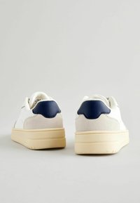 Witte sneakers met een glad leren bovenwerk, marineblauwe leren accenten op de hiel en een lichtbeige rubberen zool.