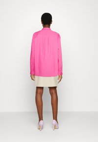 Camisola de manga longa rosa-brilhante com colarinho, pregas nas costas e punhos abotoados, combinada com uma saia bege e sapatos de salto alto lilás claro.