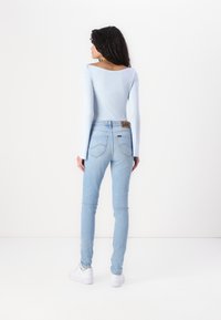 Top de manga larga azul claro combinado con jeans skinny azul claro. Los jeans presentan una etiqueta marrón en la cintura y bolsillos traseros sutiles. Zapatillas blancas.