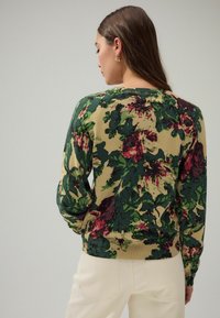 Trui met bloemenpatroon in groen, rood en beige. Beschikt over geribbelde manchetten en een zoom, met een ronde hals en een textuur gebreide afwerking.