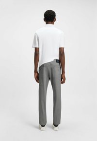 White short-sleeve polo shirt paired with gray, textured, straight-leg trousers. Dark waistband with logo detail on the back. Casual footwear visible.