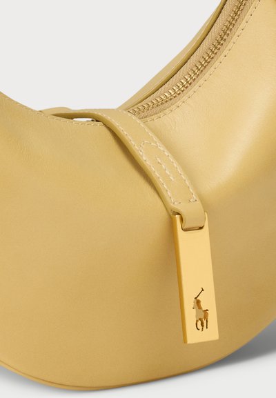Rumena usnjena torbica s ukrivljeno obliko, z zlatim zadrgo in zlatim oznako, ki vsebuje logo. Gladka tekstura in minimalističen dizajn.