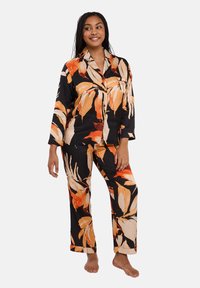 Ensemble de pyjama noir avec de grands imprimés floraux orange et crème. Le haut a un col et des manches longues ; le pantalon a une coupe droite.