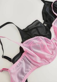 Drie bh's weergegeven: één zwart met doorzichtige kantdetails, één roze met ingewikkelde kantafwerking en een glad middenpaneel.