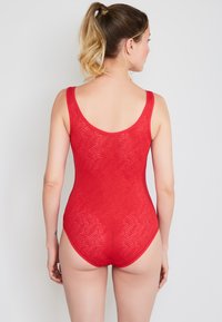 Rød badedragt lavet af tekstureret materiale med et bølget mønster. Har en rund ryg og brede stropper, der fremhæver et tætsiddende design.