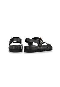Sandali in pelle nera con cinturini regolabili, dotati di borchie in metallo lungo la suola, suola in gomma piatta e design aperto sulla punta.