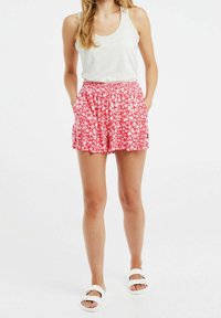 Shorts floraux rouges avec une taille élastique, présentant un motif de fleurs blanches, associés à un débardeur gris clair et des sandales blanches à enfiler.