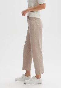 Mujer vistiendo jeans rectos de color beige claro, zapatillas blancas de caña baja y un suéter corto de punto blanco, de pie de lado.