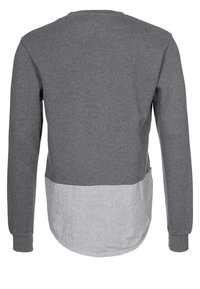 Maglia a maniche lunghe grigia con pannello inferiore di colore grigio chiaro a contrasto. Realizzata in tessuto morbido, presenta una scollatura tonda e polsini a coste.