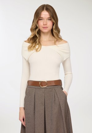 Top crema a coste con scollo a barca, abbinato a una gonna a quadri marrone con cintura, pieghe e fibbia color oro. Texture liscia e design aderente.