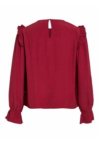 Blouse rouge à manches longues, avec des accents volantés aux épaules et une ouverture en forme de trou de serrure dans le dos. Texture lisse, coupe ample et poignets froncés.