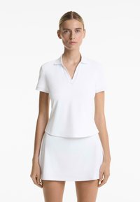 White polo shirt with a V-neck and short sleeves, paired with a matching white skirt, made of smooth, stretchable fabric.
