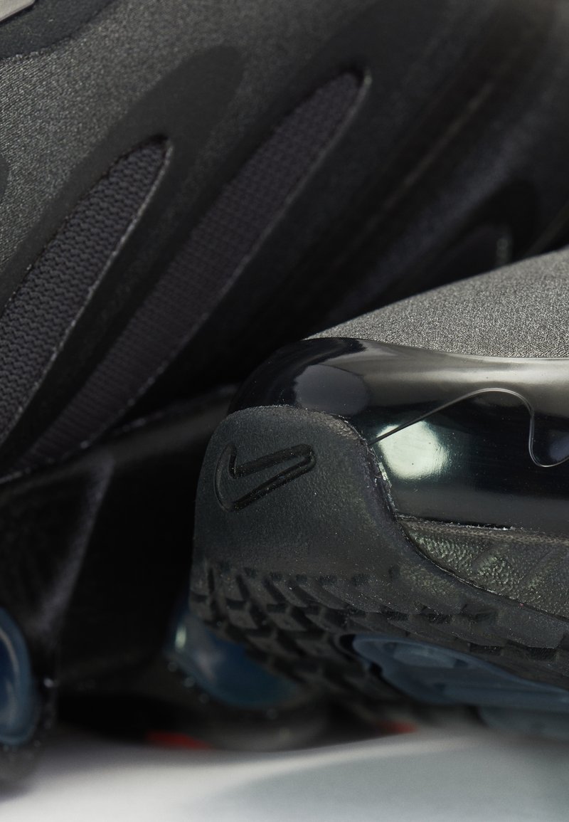 Zapatillas deportivas negras con un upper texturizado, paneles de malla, un capuchón de talón trasero brillante y una suela de goma con patrón. Logo de Nike visible.