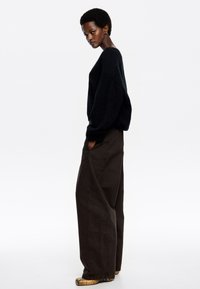 Suéter negro oversized con un acabado texturizado, combinado con pantalones de pierna ancha marrones de talle alto. Diseño hasta el suelo y calzado detallado.