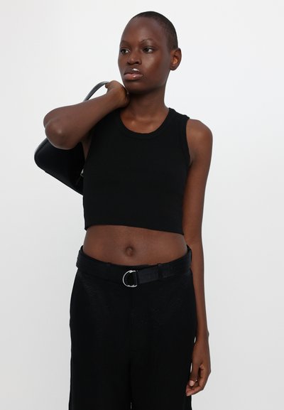Zwarte geribbelde crop top met een ronde halslijn, gecombineerd met hoge zwarte broek en een zwarte riem met een zilveren ringgesp.