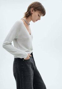 Lichtgrijze, gebreide trui met een V-hals; gecombineerd met hoge, donkere spijkerbroek. Zachte textuur zichtbaar in de stof.