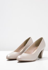 Chaussures à talons hauts beiges avec une finition en cuir texturé, bout rond et talon effilé. Design simple avec des détails de couture subtils.