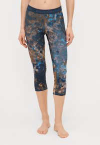 PeakPerformance capri leggings kék, barna és sötétkék batikolt mintával. Rugalmas anyagból készültek, támogató derékrésszel rendelkeznek.
