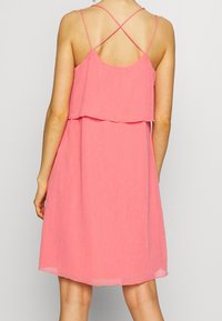 Rosa ärmelloses Kleid mit einem Schichtendesign, das einen tiefen Rücken und überkreuzte Träger aufweist. Hergestellt aus leichtem Stoff mit einer leicht strukturierten Oberfläche.